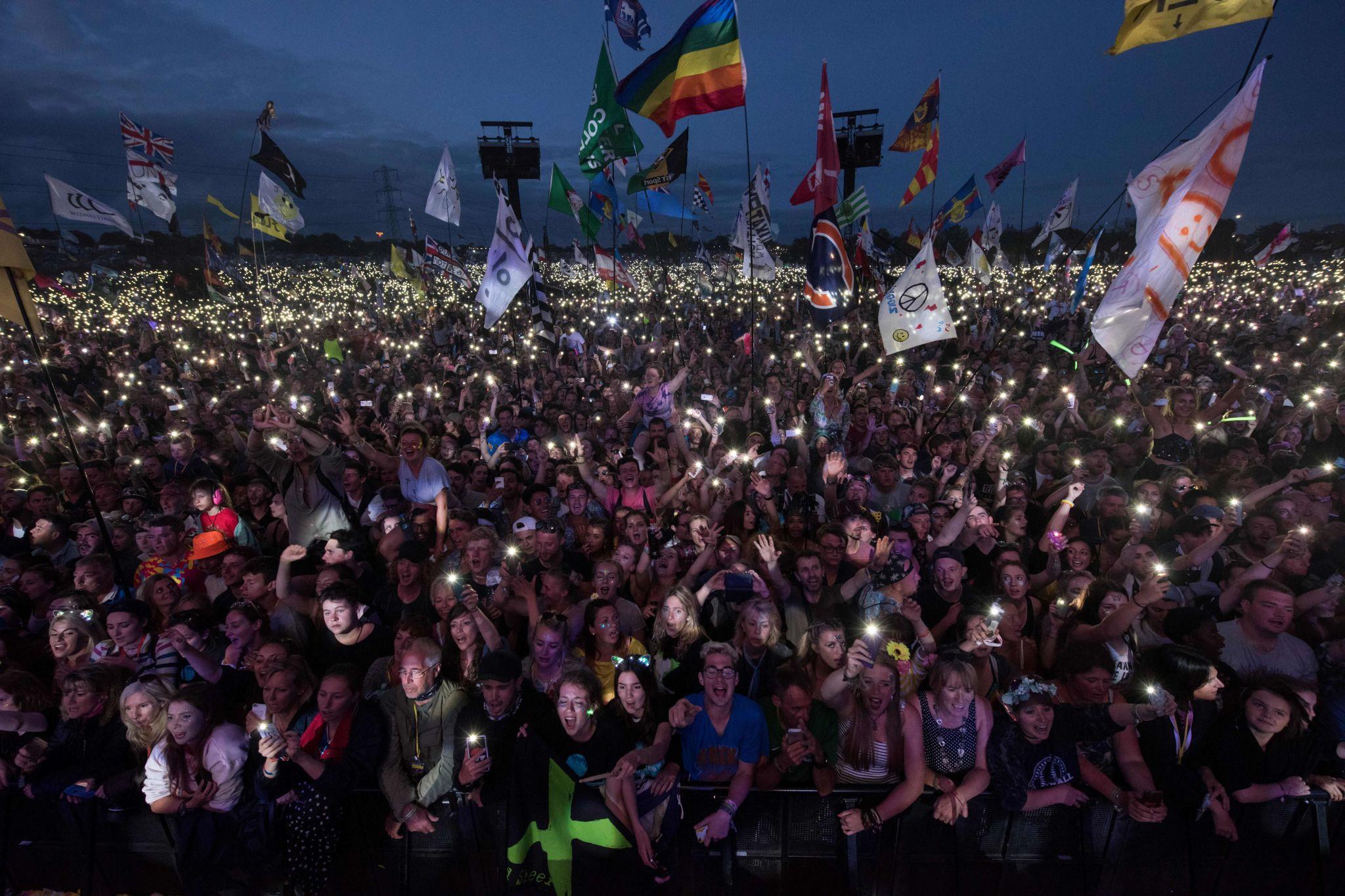Massive crowd at a European music festival with lights, flags, and a night-time atmosphere